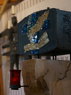 Moderner Kerzenhalter mit Glas-Mosaik, im Hintergrund Kruzifix und Wandgestaltung in der Kirche St. Hedwig in Lotte